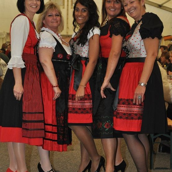 Fünf Frauen in traditioneller deutscher Kleidung, die bei einer Veranstaltung zusammenstehen und für ein Foto lächeln.