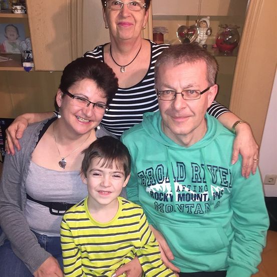 Eine Familie aus drei Personen, eine Frau, ein Mann und ein Junge, lächeln und posieren für ein Foto in einem Raum.