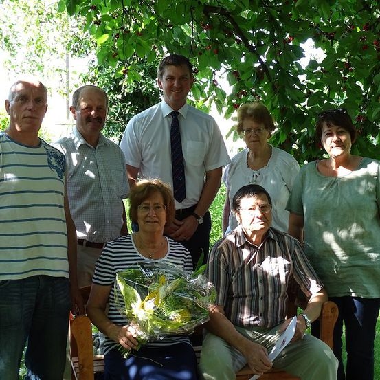 Eine Gruppe von Menschen, darunter eine Frau mit Blumen, posiert für ein Foto in einem Garten unter einem Kirschbaum.