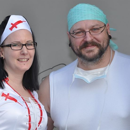 Ein Mann und eine Frau in medizinischen Kostümen, die Frau trägt eine Krankenschwestermütze und der Mann eine chirurgische Maske und ein Stirnband.