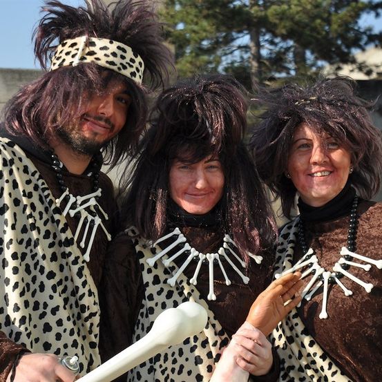 Drei Personen in Leoparden-Kostümen mit Knochenhalsbändern, die für ein Foto posieren. Der Mann links trägt eine Leoparden-Kopfbedeckung.