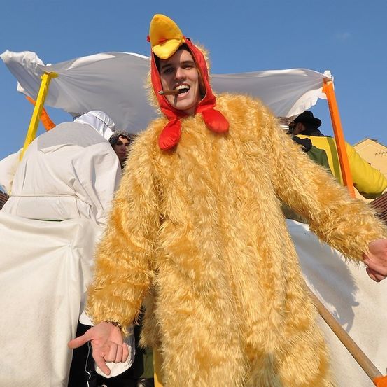 Eine Person, die als Huhn mit rotem Schnabel und gelbem flaumigen Kostüm gekleidet ist, lächelt und posiert für die Kamera.