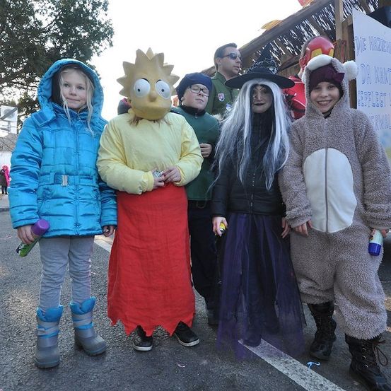 Fünf Kinder in Kostümen, zwei von ihnen als Simpsons-Charaktere verkleidet, posieren für ein Foto auf der Straße.