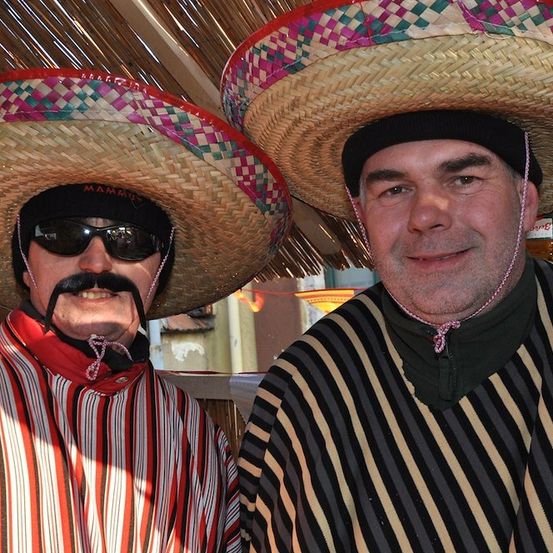 Zwei Männer in mexikanischer Kleidung, einer mit einem rot-weiß gestreiften Shirt und der andere in Schwarz-Weiß-Streifen, beide tragen Sombreros und Sonnenbrillen.