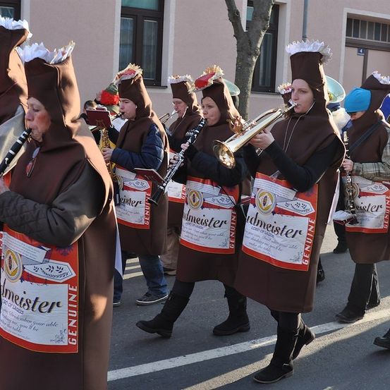 Eine Gruppe von Musikern, die in braunen Kostümen gekleidet sind, die Bierflaschen ähneln, spielen Instrumente bei einem Umzug.