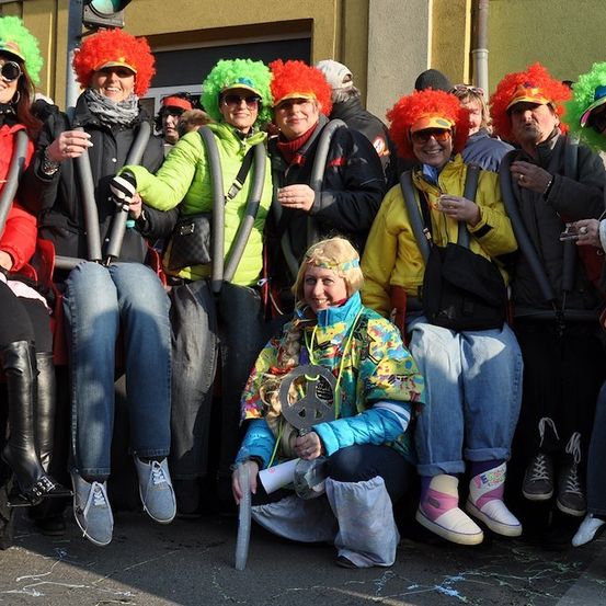 Eine Gruppe von Menschen in bunten Kostümen und Perücken posiert für ein Foto bei einer Outdoor-Veranstaltung.