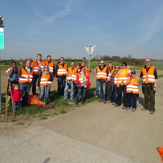 Eine Gruppe von Menschen in orangefarbenen Westen posiert für ein Foto auf einem Grasfeld mit einer Straße im Hintergrund.
