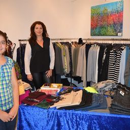 Eine Frau und ein junges Mädchen stehen vor einem Tisch mit gefalteter Kleidung und einem Gemälde an der Wand.