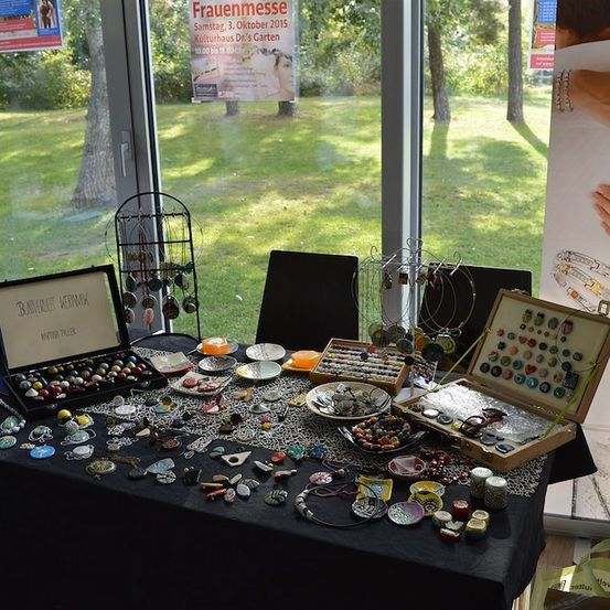 Ein Tisch mit verschiedenen Schmuckstücken zur Ausstellung, einschließlich Halsketten, Armbänder und Ringe, in einem Raum mit großen Fenstern und Blick auf ein Grasfeld aufgestellt.