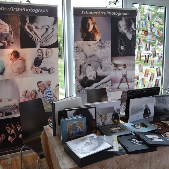 Ein Ausstellungstisch mit verschiedenen Fotoalben und gerahmten Bildern, einschließlich Familienfotos und Porträts, vor einem Hintergrund mit einer Collage von Fotos.