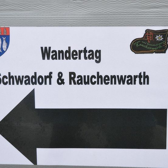 Ein Schild mit Stiefellogo und Wappen weist auf den 'Wandertag' in Schwadorf & Rauchenwarth hin.
