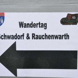 Ein Schild mit Stiefellogo und Wappen weist auf den 'Wandertag' in Schwadorf & Rauchenwarth hin.