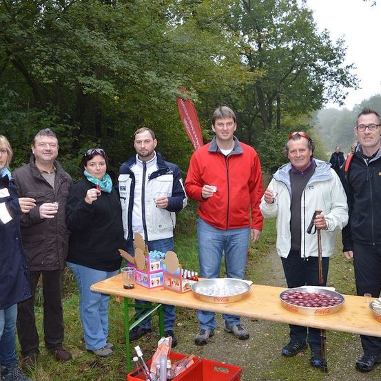 Eine Gruppe von Menschen in Winterkleidung posiert für ein Foto in einer Waldumgebung mit einem Tisch voller Coca-Cola-Produkte vor ihnen.