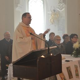 Ein Priester hält in einer Kirche eine Predigt, mit einer Kerze auf der Kanzel und einer Statue an der Wand.