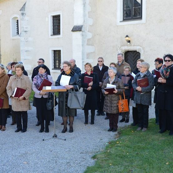 Ein Chor älterer Personen in Winterkleidung steht vor einem Gebäude, hält Gesangbücher und singt.