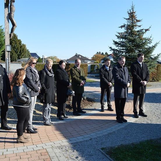 Eine Gruppe von Menschen in formeller Kleidung steht in einem Kreis um ein Kreuz in einem Park.