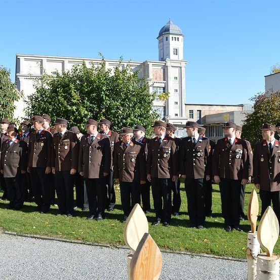 Eine Gruppe uniformierter Personen, möglicherweise Militäroffiziere, steht in Formation auf einem Rasen mit Gebäuden im Hintergrund.