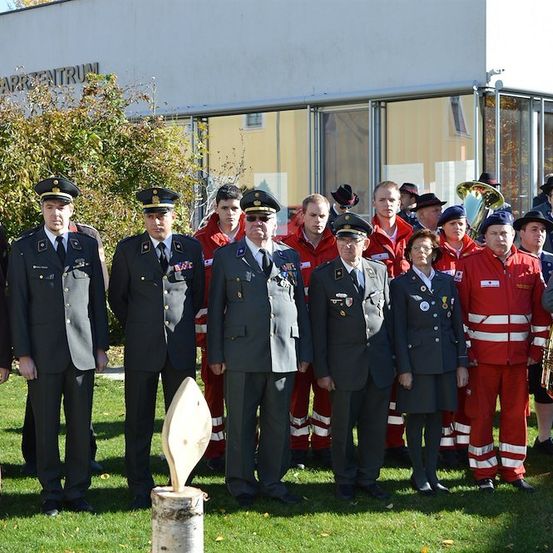 Eine Gruppe von Menschen in Uniform, einschließlich Militärangehöriger und Feuerwehrleute, steht vor einem Gebäude. Sie posieren für ein Foto.