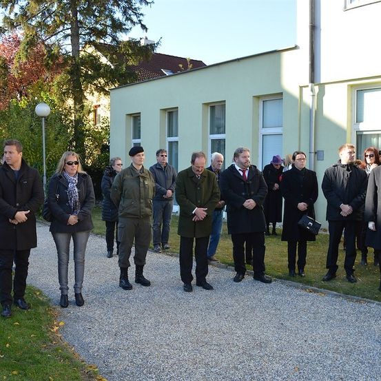 Eine Gruppe von Menschen in formeller Kleidung steht in einer Reihe vor einem Gebäude, möglicherweise während einer formellen Veranstaltung.