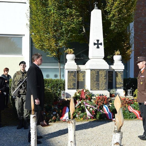 Eine feierliche Zeremonie an einem Kriegerdenkmal mit Militärangehörigen und Zivilisten bei klarem Himmel.