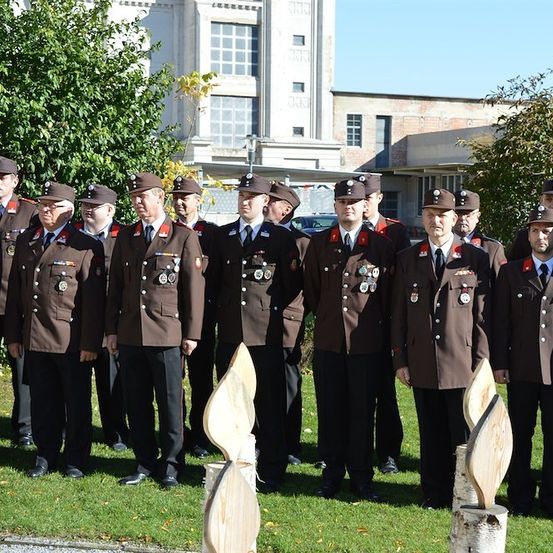 Eine Gruppe uniformierter Männer, möglicherweise Militärangehörige, steht in einer Reihe auf einem Rasen mit einem Gebäude im Hintergrund.