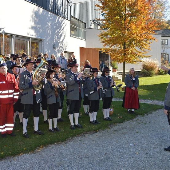 Eine Gruppe von Musikern in traditionellen Uniformen spielt vor einem Gebäude. Sie halten verschiedene Blech- und Holzblasinstrumente.