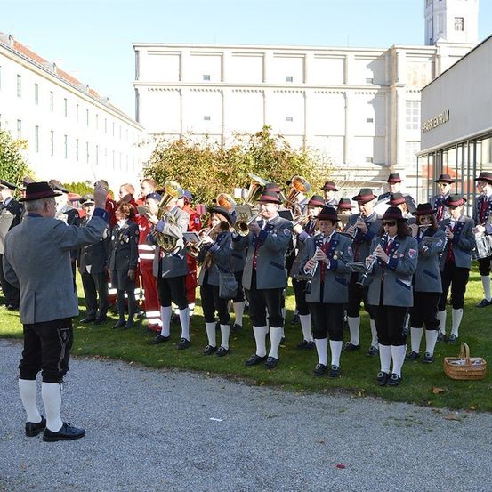 Eine Blaskapelle in traditionellen Uniformen spielt vor einem großen Gebäude an einem sonnigen Tag.