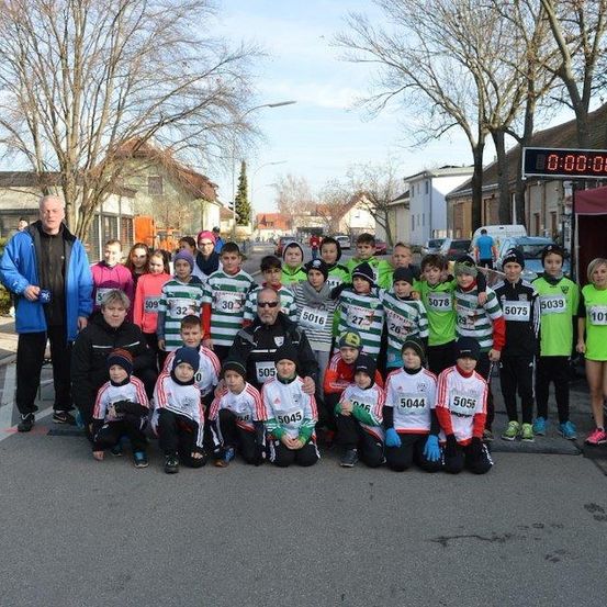 Eine Gruppe von Kindern und Erwachsenen mit nummerierten Shirts posiert für ein Foto auf einer Straße. Eine digitale Uhr zeigt 0:00:00.