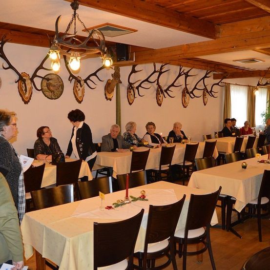 Eine Gruppe von Menschen sitzt in einem Restaurant mit Holzbalken und Geweihen an der Wand.