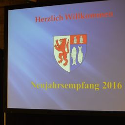 Ein Präsentationsfolie mit blauem Hintergrund, die einen deutschen Text 'Herzlich Willkommen' und ein Wappen mit einem roten Löwen und Fisch, zusammen mit dem Jahr '2016' zeigt.