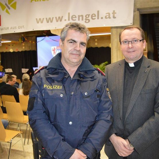 Zwei Männer stehen nebeneinander vor einer Menschenmenge, einer ist Polizist und der andere ist Priester.