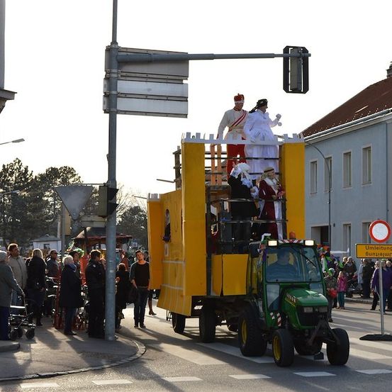 Ein Umzug mit Menschen in Kostümen, die auf einem gelben Traktor in einem Stadtplatz fahren.