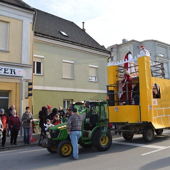 Ein Umzug mit einem Traktor-Wagen, Menschen in mittelalterlichen Kostümen und eine Menge, die vom Bürgersteig zusieht.