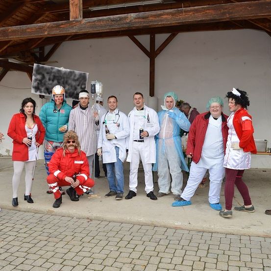 Eine Gruppe von Menschen in verschiedenen Kostümen, einschließlich Laborkitteln und Schutzausrüstung, posiert für ein Foto in einer Scheune.