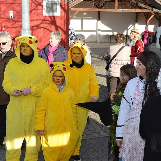 Drei Erwachsene in Pikachu-Kostümen stehen zusammen in einem öffentlichen Bereich mit anderen Menschen in verschiedenen Kostümen.