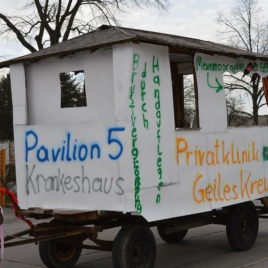 Ein weißer Anhänger mit Graffiti, beschriftet mit 'Pavillon 5' und 'Krankenhaus', am Straßenrand geparkt.