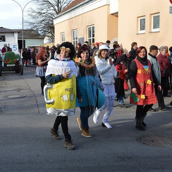 Eine Gruppe von Menschen in Kostümen, darunter ein Bierkrug, geht vor einem Gebäude die Straße entlang.