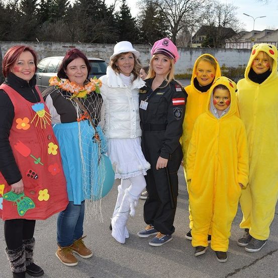 Eine Gruppe von Menschen in verschiedenen Kostümen, darunter eine Polizistin, ein Blumenkleid und Pikachu-Outfits, steht auf einem Parkplatz.