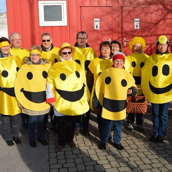 Eine Gruppe von Menschen in gelben Smiley-Kostümen steht vor einem roten Gebäude.