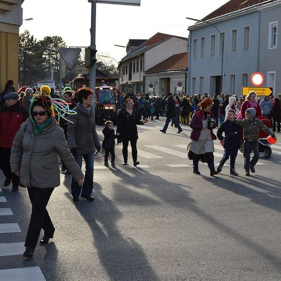 Eine Menschenmenge, einige in Kostümen, geht über eine Straße mit einem Zebrastreifen. Im Hintergrund befinden sich Gebäude und ein Fahrzeug.