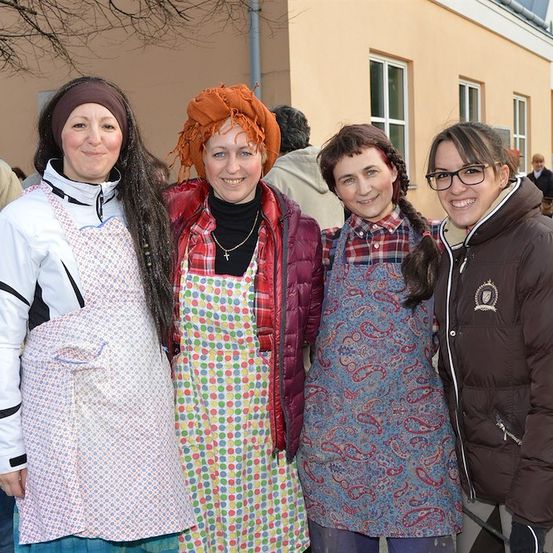Vier Frauen in Schürzen und lächelnd vor einem Gebäude für ein Foto.