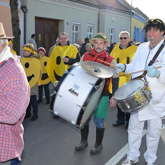 Eine Gruppe von Menschen in gelben Kostümen mit Smiley-Gesichtern spielt auf der Straße Trommeln.