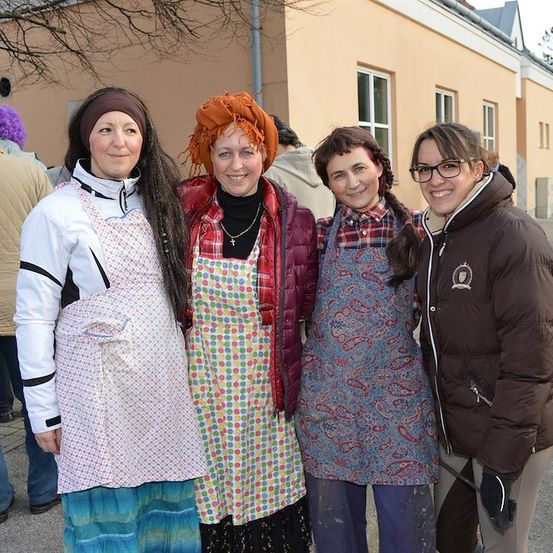 Vier Frauen in Schürzen, stehen vor einem Gebäude und lächeln für ein Foto.