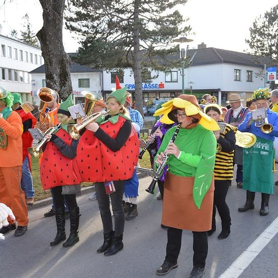 Eine Gruppe von Musikern in Obstkostümen spielt auf der Straße, einer spielt Klarinette und andere spielen Blechblasinstrumente.