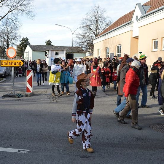 Eine Gruppe von Menschen in Kostümen, die auf einer Straße mit Gebäuden und Straßenschildern im Hintergrund eine Parade abhalten.