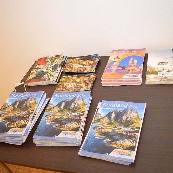 Eine Sammlung von Reiseprospekten auf einem Holztisch, einschließlich 'Europa 2016', 'Atlantis 2016' und mehrere 'Nordland 2016'.