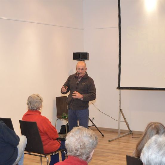 Ein Mann hält eine Präsentation in einem Raum mit einer Projektionsleinwand und einem Mikrofon.