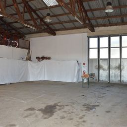 Ein leerer Lagerraum mit weiß bedeckten Tischen, einem Fahrrad auf dem Balkon und einem Feuerlöscher in der Nähe der Tür.