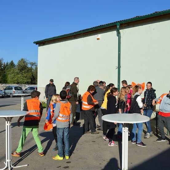 Eine Gruppe von Menschen in orangefarbenen Westen steht vor einem Gebäude mit einem grünen Dach, einige unterhalten sich und andere schauen sich um.