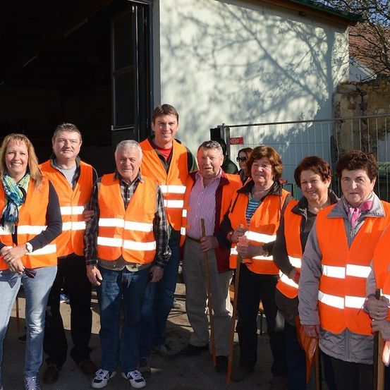 Eine Gruppe von Menschen in orangefarbenen Sicherheitswesten steht vor einem Gebäude. Sie lächeln und scheinen für ein Foto zu posieren.